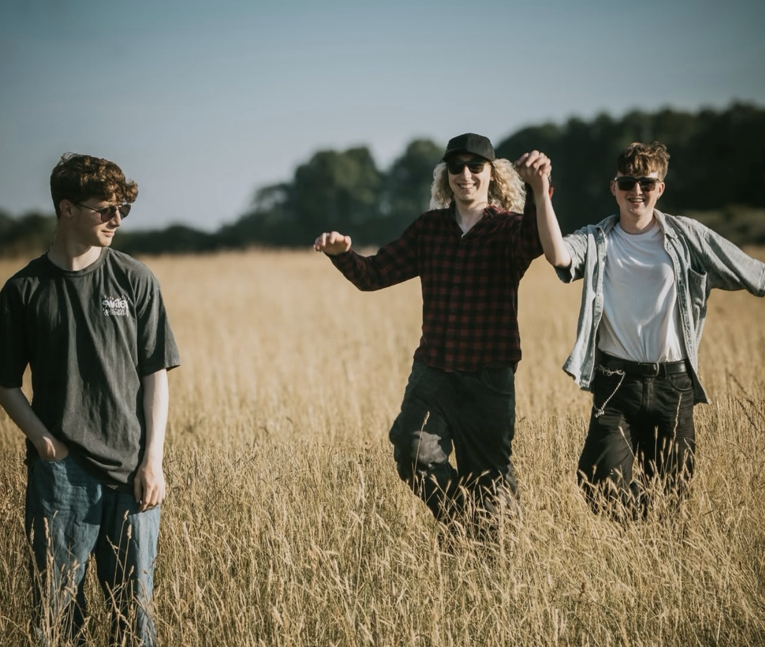 Revivalry's three members walking through a sunlit field of long golden grass