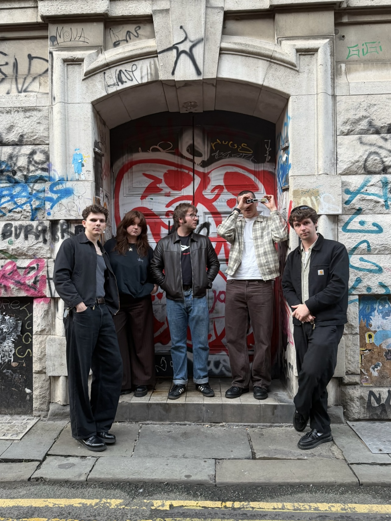 Sun in Splendour's five members standing in a graffiti-covered doorway on a Manchester street