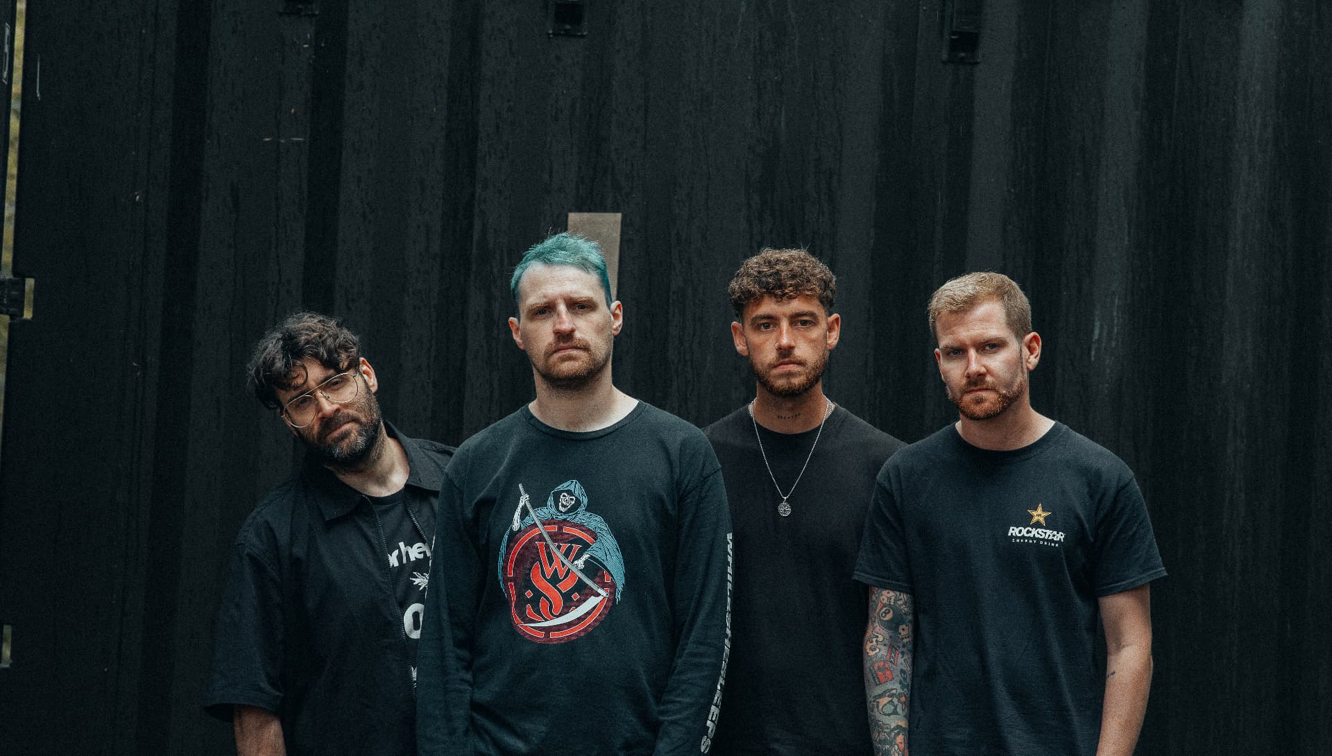 Delta Signal — four members in black against a dark slatted wall, one with dyed teal hair
