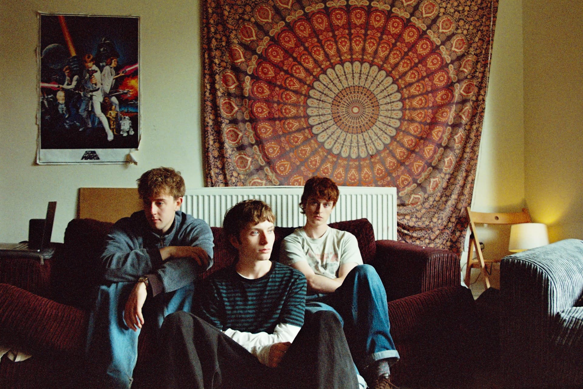 Split the Ticket's three members sitting on a sofa beneath a patterned wall hanging