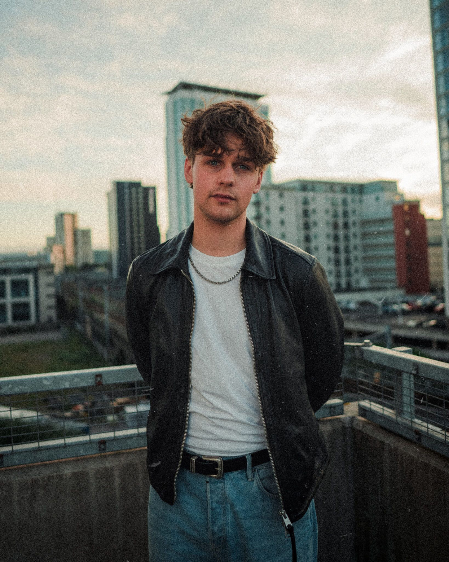 Ben Ellis in a black leather jacket and white tee on a Cardiff rooftop at dusk