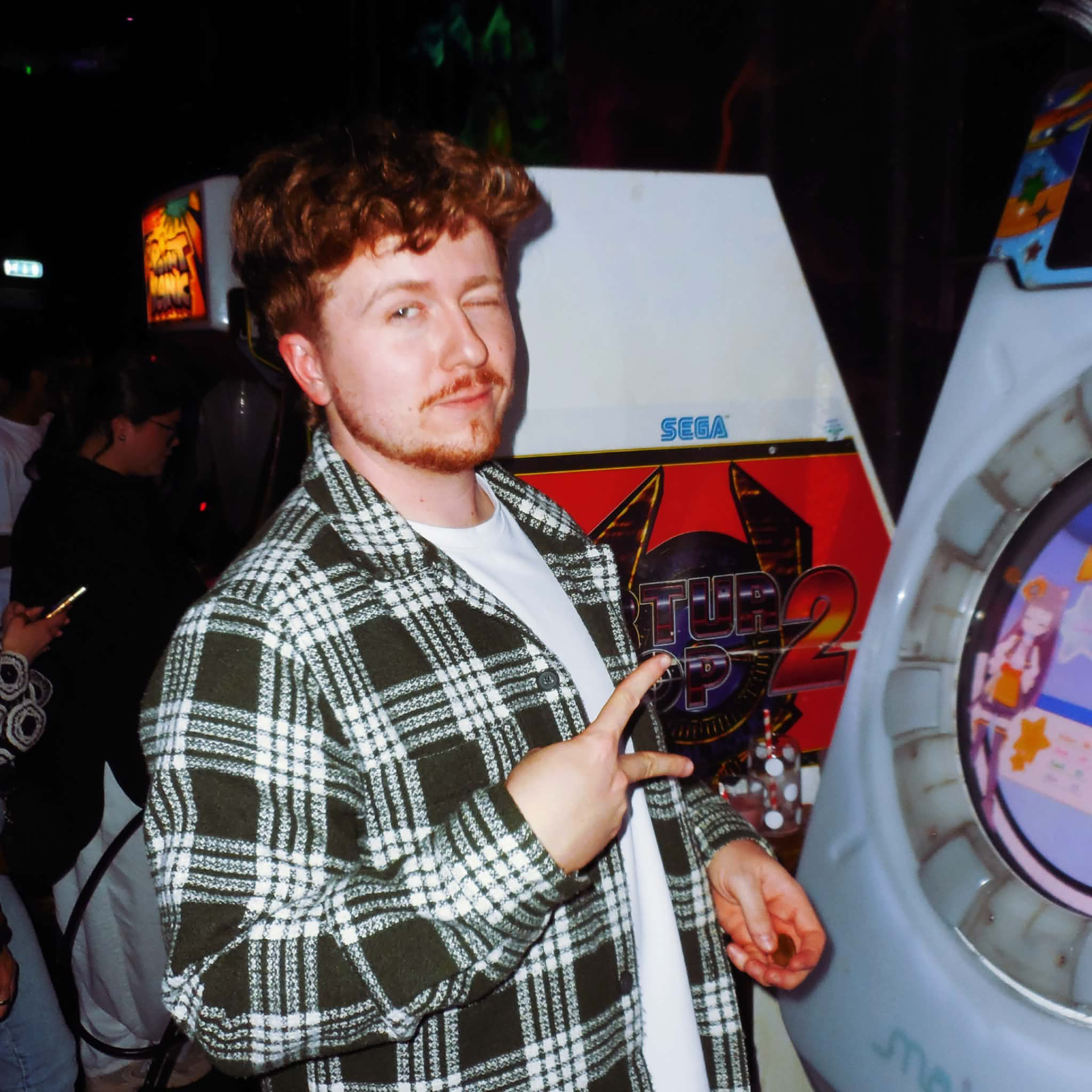 James winking and flashing a peace sign in front of a wall of arcade machines